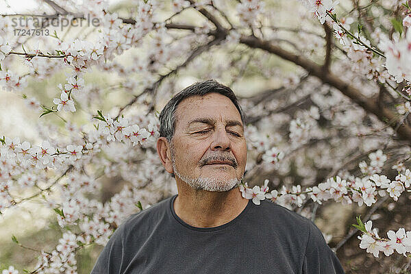 Mann mit geschlossenem Auge vor einem Blumenbaum