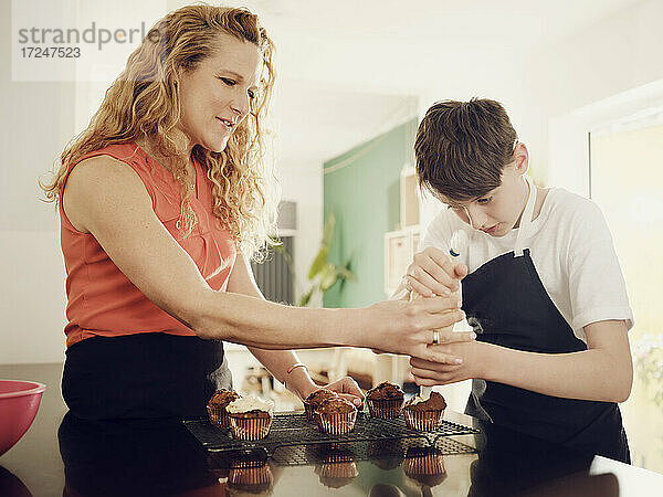 Mutter bringt ihrem Sohn bei  Muffins mit einem Spritzbeutel in der Küche zu Hause zu glasieren