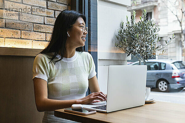Nachdenkliche Frau schaut weg  während sie einen Laptop im Café benutzt