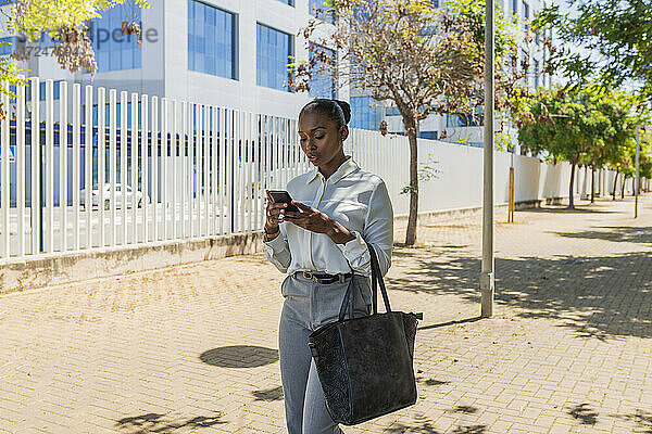 Mittlerer erwachsener Unternehmer  der ein Mobiltelefon benutzt  während er auf dem Gehweg steht
