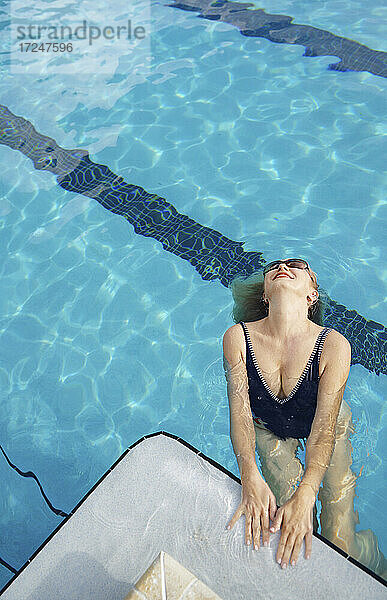 Reife Frau trägt ein Stück Badeanzug lächelnd im Schwimmbad
