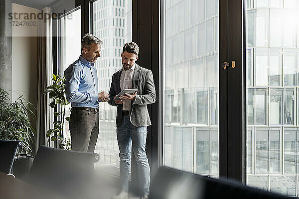 Geschäftsleute besprechen einen Plan über eine digitale Tafel am Fenster am Arbeitsplatz