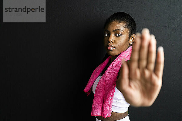 Selbstbewusste Frau mit Stopp-Geste im Stehen vor schwarzem Hintergrund