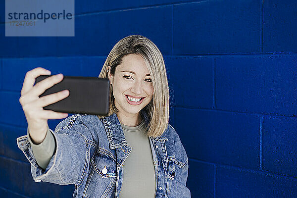 Frau nimmt Selfie durch Smartphone durch blaue Wand