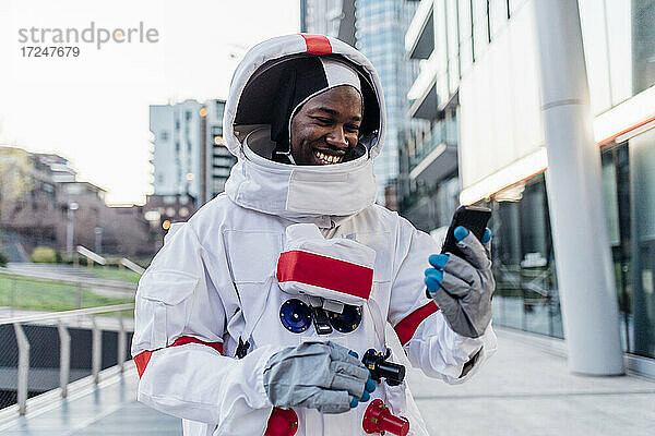 Lächelnder männlicher Astronaut  der ein Mobiltelefon auf einem Fußweg benutzt