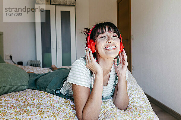 Schöne Frau mit Kopfhörern  die lächelnd auf dem Bett liegt