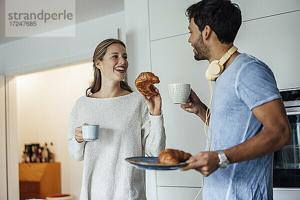 Glückliches junges Paar mit Croissant und Kaffeetasse in der Küche