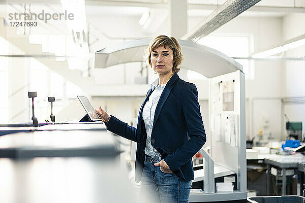 Geschäftsfrau mit Hand in der Tasche  die vor einer digitalen Tafel in einer Fabrik steht