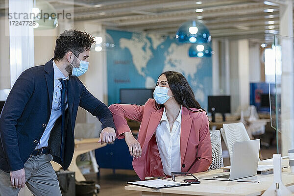 Männliche und weibliche Unternehmer stoßen sich während der Pandemie im Büro die Ellbogen an