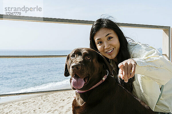 Schöne Frau mit Labrador-Hund  der auf einen sonnigen Tag am Strand zeigt