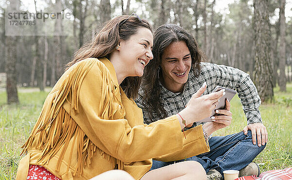 Fröhlicher Mann und Frau schauen auf ein digitales Tablet während einer Party im Wald