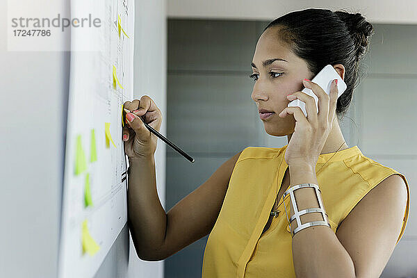 Junge Geschäftsfrau  die bei der Arbeit im Büro mit ihrem Mobiltelefon telefoniert
