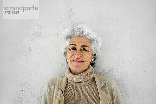 Frau mit grauem Haar lächelnd vor einer Wand