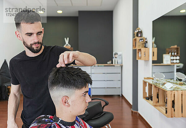 Männlicher Friseur kämmt das Haar eines Kunden  während er eine Frisur im Salon macht