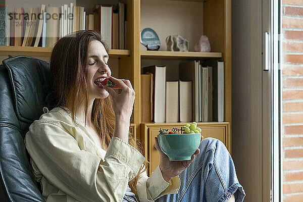 Schöne Frau isst Früchte  während sie auf einem Stuhl zu Hause sitzt