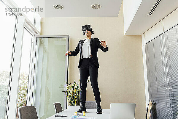 Junge Geschäftsfrau  die einen Virtual-Reality-Simulator benutzt  während sie auf einem Schreibtisch im Büro steht