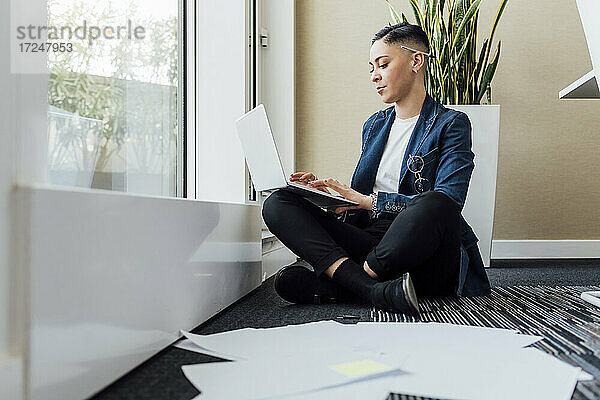 Weibliche Fachkraft  die einen Laptop benutzt  während sie auf dem Büroboden sitzt