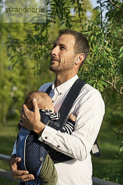 Aufmerksamer Vater kümmert sich im Park um seinen Sohn in der Babytrage