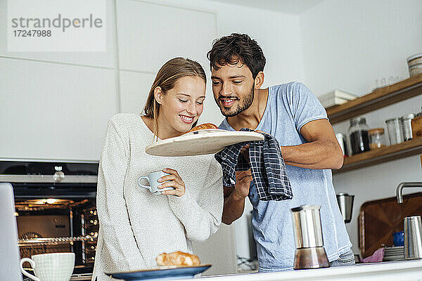 Mann zeigt seiner Freundin ein frisch gebackenes Croissant in der Küche zu Hause