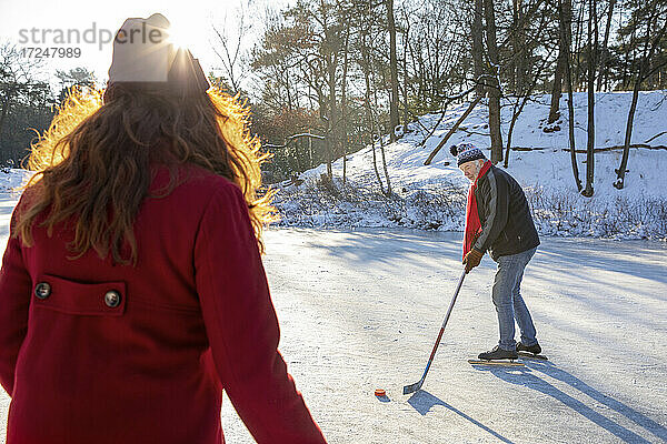 Älterer Mann spielt Eishockey mit Frau auf Schnee im Winter