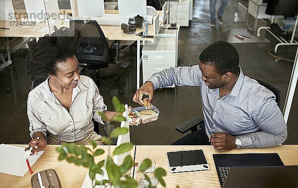 Männliche und weibliche Mitarbeiter teilen sich in der Mittagspause im Coworking-Büro ein Sandwich