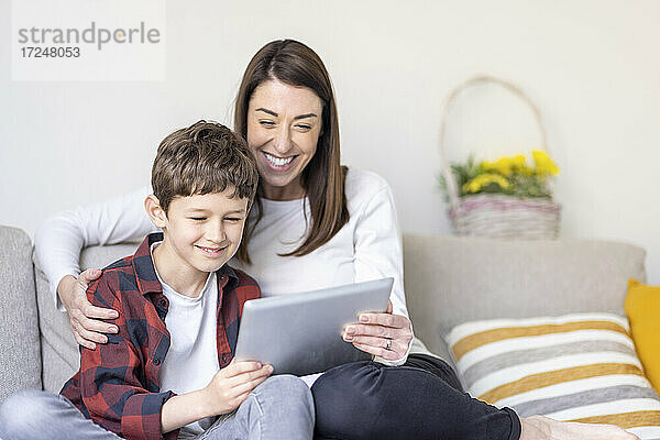 Lächelnder Junge und Mutter verwenden digitales Tablet auf dem Sofa zu Hause