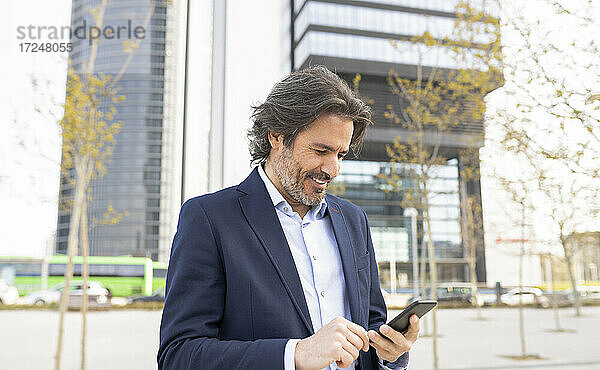 Lächelnder Geschäftsmann mit Smartphone in der Stadt