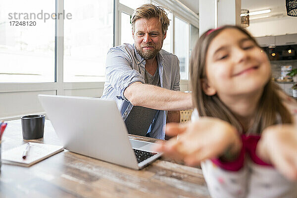 Geschäftsmann schaut auf einen Laptop  während er neben seiner spielenden Tochter zu Hause sitzt