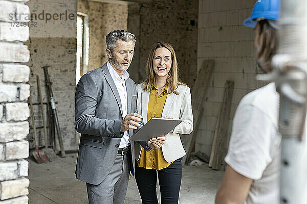Männlicher Architekt mit digitalem Tablet  der neben einer lächelnden Kollegin auf der Baustelle steht