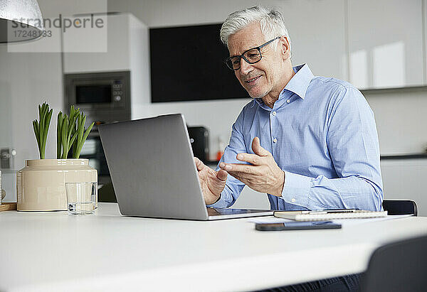 Lächelnder Unternehmer  der über einen Laptop im Büro ein Videogespräch führt