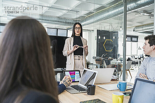 Weibliche Fachkraft im Gespräch mit männlichen und weiblichen Unternehmern während eines Treffens im Coworking-Büro
