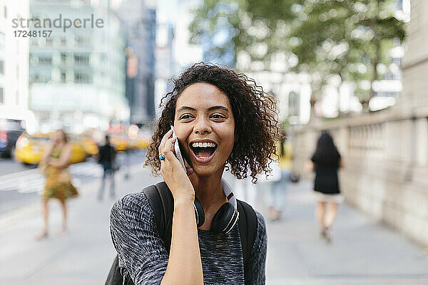 Frau lacht  während sie in der Stadt mit einem Smartphone telefoniert
