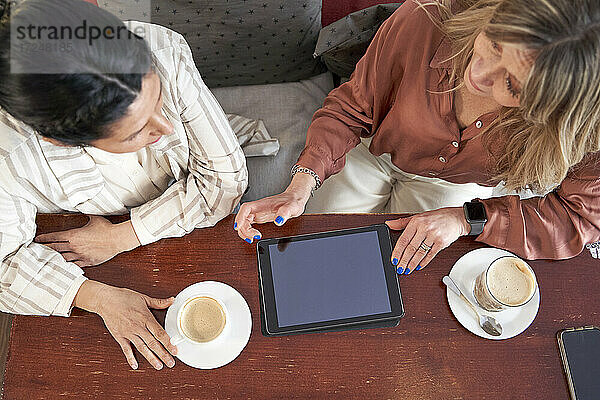 Unternehmerinnen mit digitalem Tablet diskutieren in der Cafeteria