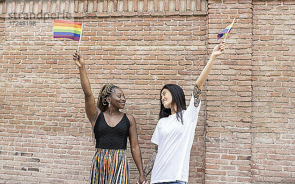 Lesbisches Paar schwenkt Regenbogenflagge an der Wand