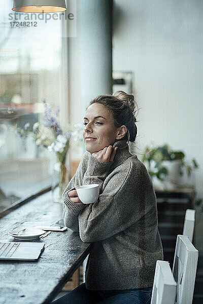 Nachdenkliche Unternehmerin mit Kaffeetasse am Fenster eines Cafés