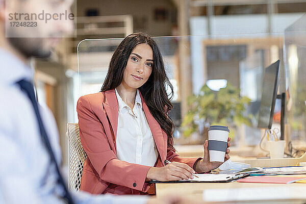 Geschäftsfrau hält Kaffee wiederverwendbaren Kaffeebecher während der Arbeit am Schreibtisch von männlichen Unternehmer im Büro