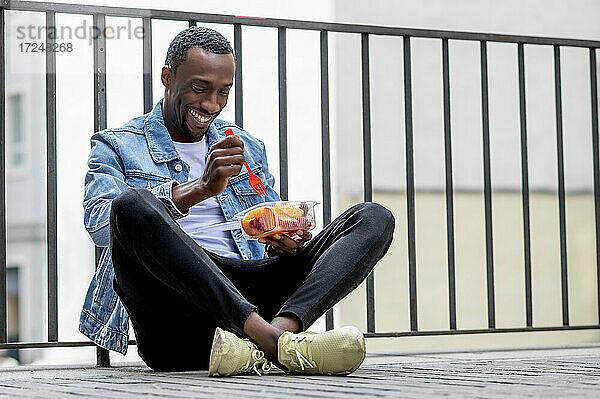 Junger Mann isst gesundes Mittagessen im Schneidersitz auf dem Fußweg