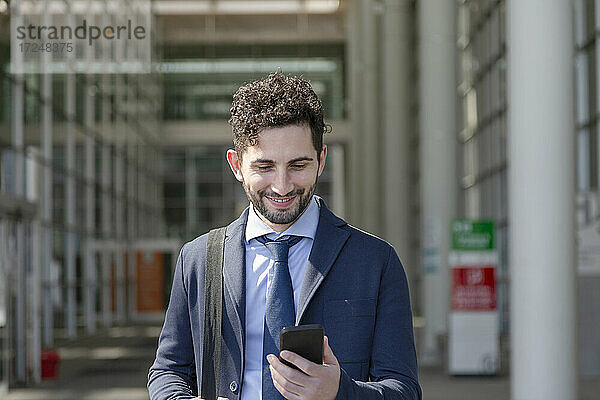 Lächelnder Unternehmer  der an einem sonnigen Tag ein Mobiltelefon benutzt