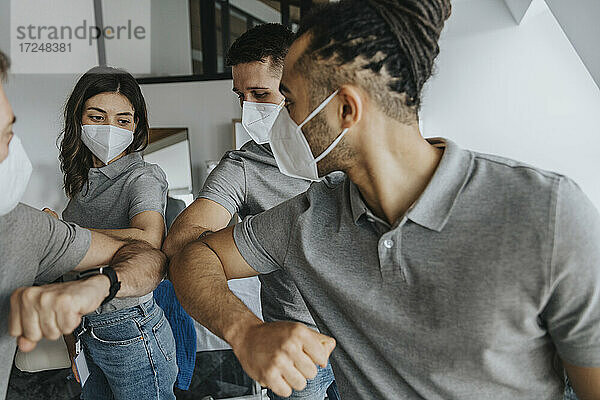 Männliche und weibliche Physiotherapeuten mit Gesichtsschutzmasken beim Ellbogenstoßen