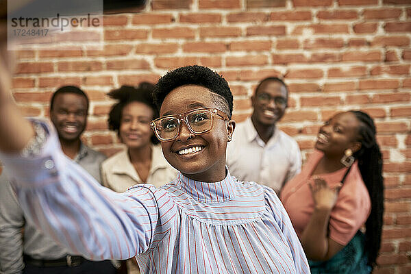 Lächelnde Geschäftsfrau  die ein Selfie mit Kollegen in einem Coworking-Büro macht
