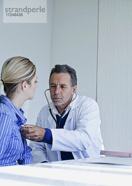 Männlicher Arzt  der eine Patientin mit Stethoskop im Krankenhaus untersucht