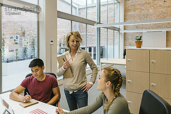 Lächelnde weibliche Fachkräfte  die mit einem männlichen Kollegen in einem Coworking-Büro diskutieren