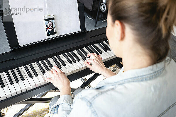 Mittlere erwachsene Frau bei einem Videoanruf  während sie zu Hause Klavier übt
