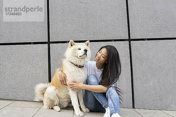 Mittlere erwachsene Frau sitzt mit Akita-Hund an der Wand