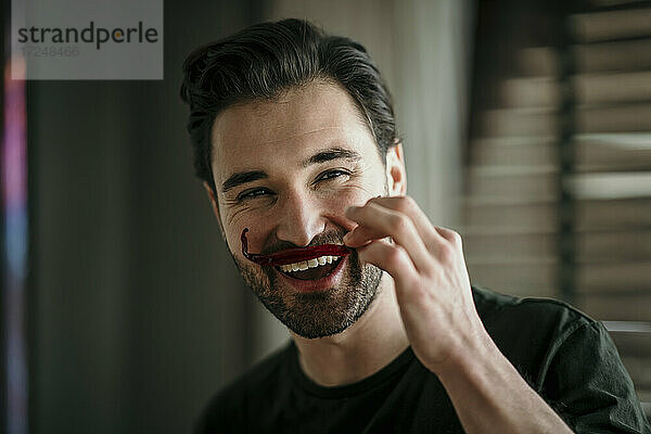 Lächelnder Mann imitiert Schnurrbart mit rotem Chili