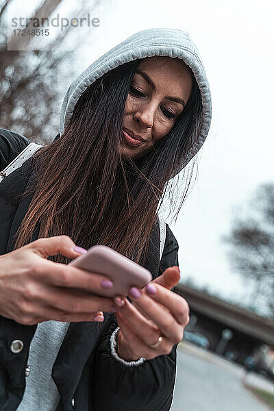 Frau in Kapuzenjacke lächelt  während sie ein Smartphone benutzt