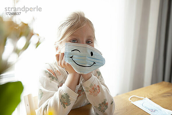 Mädchen hält Smiley-Maske zu Hause
