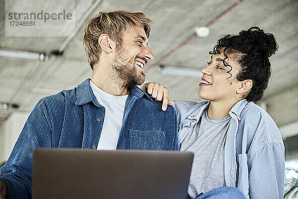 Lächelnder Mann mit Laptop  der seine Freundin auf dem Dachboden betrachtet