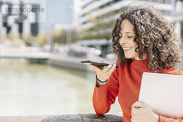 Frau sendet Sprachnachrichten über ihr Handy  während sie ihren Laptop am Geländer festhält