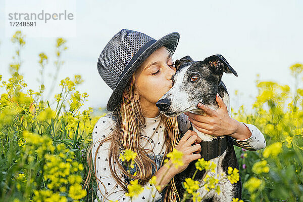 Mädchen mit geschlossenen Augen küsst Hund auf einem landwirtschaftlichen Feld